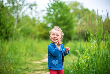 Little girl plays on nature against the background of spring greenery.