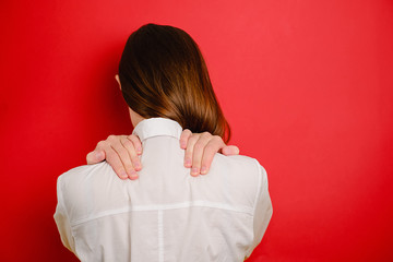 Rear close up view at young woman isolated on red studio background massage back having spasm or...
