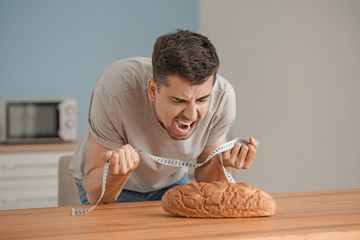 Young man suffering from anorexia with bread and measuring tape in kitchen