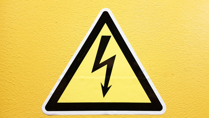 safety sign yellow and black glued on a yellow wall. High voltage lightning in a triangle caution caution danger electricity death.