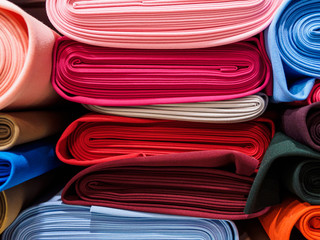 Rolls of bright multicolored fabric close-up. Many different fabrics are rolled up and lying on the...