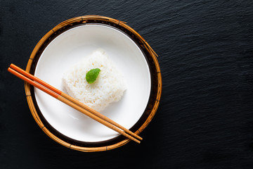 Asian Food concept cooked Thail jasmine rice long grain rice in ceramic bowl and bamboo tray on black slate board background with copy space
