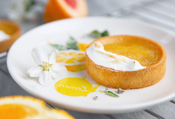 Citrus tartlet on the white plate decorated with painted lemon and white flower on it
