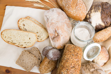 Toasts, loafs and buns of traditional wheat and rye bread, burlap sack, ears and flour. Top view. Wooden table background. Bakery or pastry concept