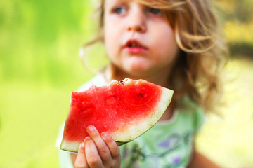 cute little girl holding a piece of watermelon close in the garden in summertime