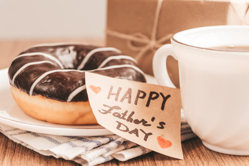 Gift box with a tag, cup of coffee or tea and chocolate donut. Father's day or birthday concept.