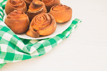 Close up of hot fresh homemade French buns cinnabones with cinnamon, tasty homemade dessert on white plate on wooden table with green tablecloth. Copyspace, selective focus