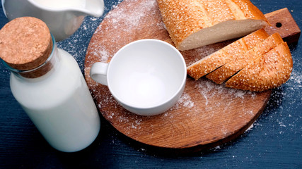 Close up of pouring milk in white cup in a wooden background next to bread.