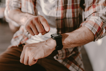 Hipster young man uses his smart watch. Checking the message or calls. Man in plaid shirt. Modern life. Black smart watches. Millennial. Hipster using all modern technologies. Era of modern gadgets.