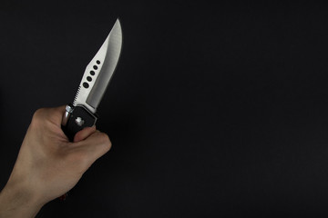 The man is holding a shiny and sharp hunter knife with his hand on the black background. Hunting, fight, combat, weapon concept photo.