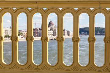 View of the building of the Hungarian Parliament and the Danube River through the fence of the bridge. Budapest, Hungary. Sunny summer day.
