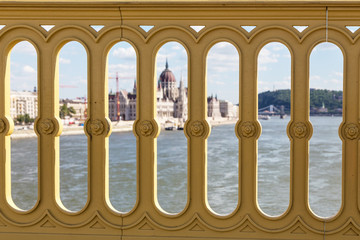 Fototapeta premium View of the building of the Hungarian Parliament and the Danube River through the fence of the bridge. Budapest, Hungary. Sunny summer day.