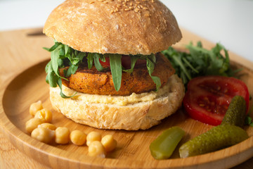 Vegan falafel hummus burger with homemade sourdough bun, tomatoes, pickled cucumbers and arugula in a wooden plate