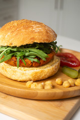 Vegan falafel hummus burger with homemade sourdough bun, tomatoes, pickled cucumbers and arugula in a wooden plate