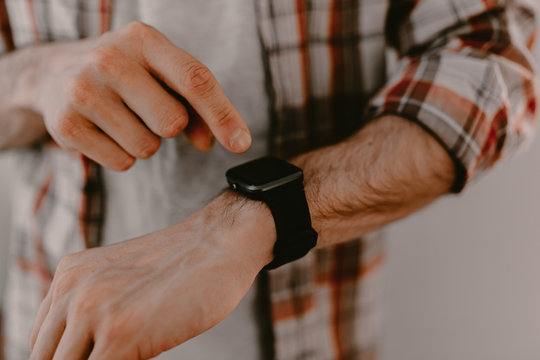 Hipster young man uses his smart watch. Checking the message or calls. Man in plaid shirt. Modern life. Black smart watches. Millennial. Hipster using all modern technologies. Era of modern gadgets. - Powered by Adobe