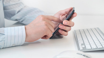 Man holding smartphone in the hand and typing message on working place table.