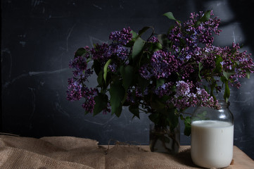 Fresh milk in a pot and a bouquet of flowers. Rural still life with flowers and milk.