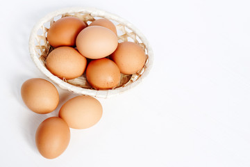 Brown chicken eggs in a straw basket on white wooden background. Top view with copy space.