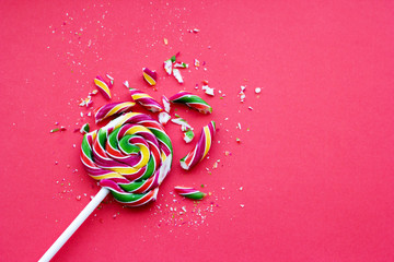 Broken in pieces candy on a stick. Smashed lollipop on pink background, top view with copy space.