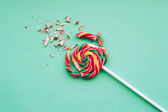Broken in pieces candy on a stick. Smashed lollipop on green background