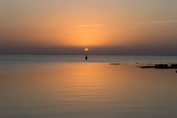 夕日のオレンジ色が反射した穏やかな海で釣りをする人