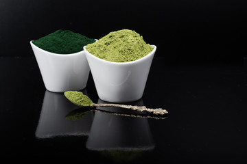 An isolated tablespoon of dried organic wheat grass and spirulina powder, on white rustic background