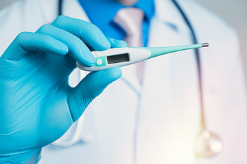 Close up view of thermometer in rubber blue glove dressed hand, man chest in white medical robe on a blurred background with stethoscope