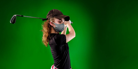 Close-up of a girl playing golf with golf club and protection mask isolated on green background, banner image	