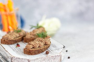 Fresh homemade chicken liver pate with carrots, onions and butter. Garnished with a sprig of dill. Lubricated on bread. On a gray background under concrete.