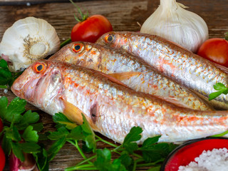red mullet on an old wooden board background with typical ingredients of an Italian recipe 