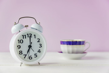 morning wake up. White alarm clock and cup of tea or coffee on white table with copy space.