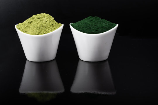 An isolated tablespoon of dried organic wheat grass and spirulina powder, on white rustic background