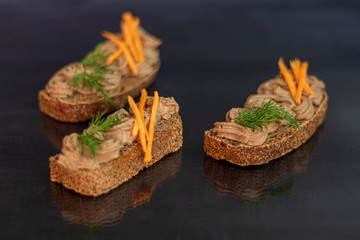 Fresh homemade chicken liver pate with carrots, onions and butter. Garnished with a sprig of dill. Lubricated on bread. On a black background.