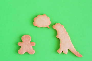 Homemade shortbread cookies in shapes of dinosaur and man with callout cloud on green background, top view.