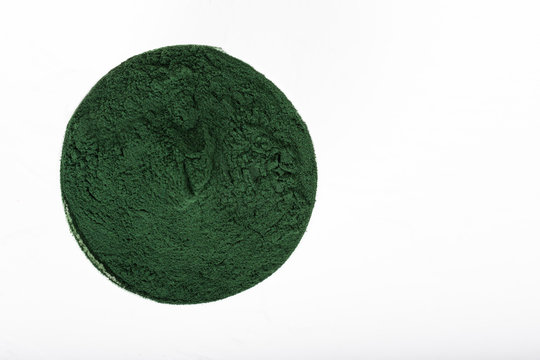An isolated tablespoon of dried organic spirulina algae powder, on white or rustic background.