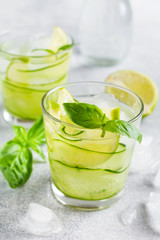 Summer homemade lemonade made from lime, lemon, cucumber and basil with ice in glass on an old concrete background. Selective focus.