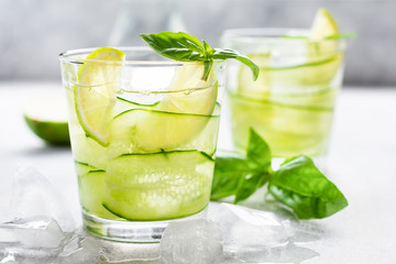 Summer homemade lemonade made from lime, lemon, cucumber and basil with ice in glass on an old concrete background. Selective focus.