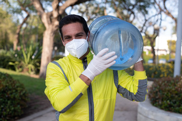 Delivery man employee in yellow  t-shirt uniform face mask gloves hold bottel of water isolated outdoor Service quarantine pandemic coronavirus virus 2019-ncov concept