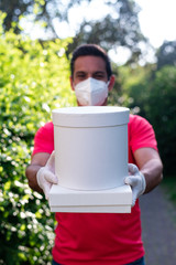 Delivery man employee in red  t-shirt uniform face mask gloves hold empty cardboard box pizza isolated on outdoor green background Service quarantine pandemic coronavirus virus 2019-ncov concept