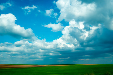 Cielo azul con nubes sobre campo verde.