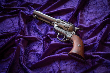Antiguo revólver del oeste con cachas marrones sobre terciopelo morado.