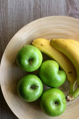 Wooden bowl with green apples and bananas on a table. Top view.