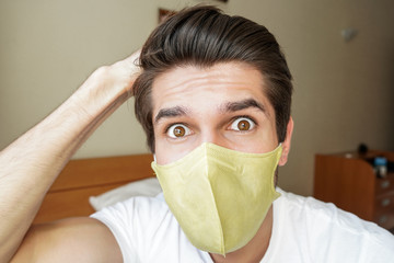 Portrait of a young handsome man wearing a face mask with a shocked emotion in his bedroom 