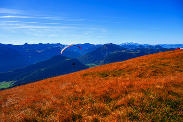 Orange meadow and blue mountains with paraglider.