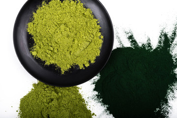 An isolated tablespoon of dried organic wheat grass and spirulina powder, on white rustic background