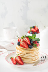 Stack of homemade little pancakes with honey, fresh strawberries and sauce on light wooden background. Selective focus.