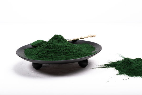An isolated tablespoon of dried organic spirulina algae powder, on white or rustic background.
