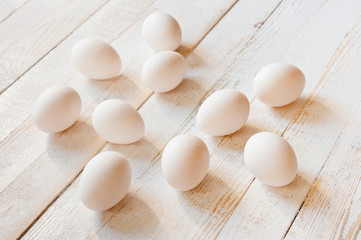 White chicken eggs lying on a white painted wooden surface. Background for livestock products.