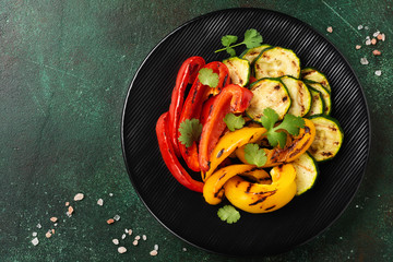 Grilled vegetables pieces of zucchini, red and yellow pepper and bouquet of cilantro on plate, salad on bbq grill rack over charcoal. Top view. Barbecue concept
