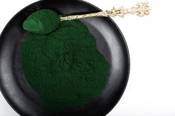 An isolated tablespoon of dried organic spirulina algae powder, on white or rustic background.